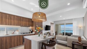 A modern kitchen with a central island, a dining area with chairs, a sofa, and a TV in a living room. - Beatiful Oceanview 1 BR Condo - Pool - Beach (Puerto Vallarta)