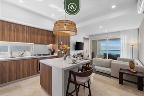 Una cocina moderna con una isla central, un comedor con sillas, un sofá y una televisión en la sala.