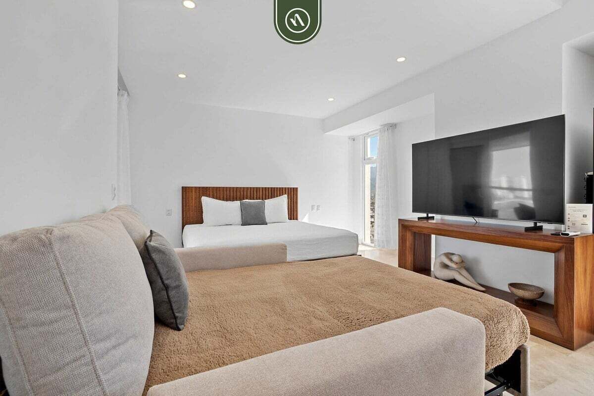 A modern hotel room with a large bed, a sofa, a TV, and a wooden console.