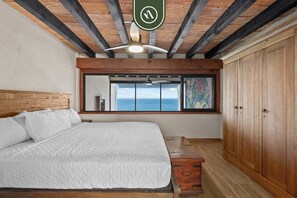A bedroom with a bed, a window with a view, a ceiling fan, and wooden beams. - Oceanfront 2 BR Condo With Spectacular View - Pool (Puerto Vallarta)