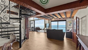 Un espaiós saló amb terra de fusta, una escala amb barana decorativa, vista al mar i un gran finestral.