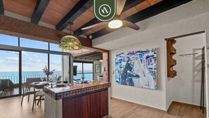 Una habitació àmplia amb un gran finestral que dona al mar, un sostre de fusta i una zona de bar amb un rebedor de rajola.
