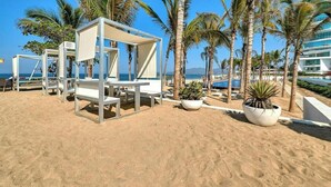 A beach area with white lounge chairs, palm trees, and a pool. - 2BR With Private Balcony - Oceanfront Building (Nuevo Nayarit)