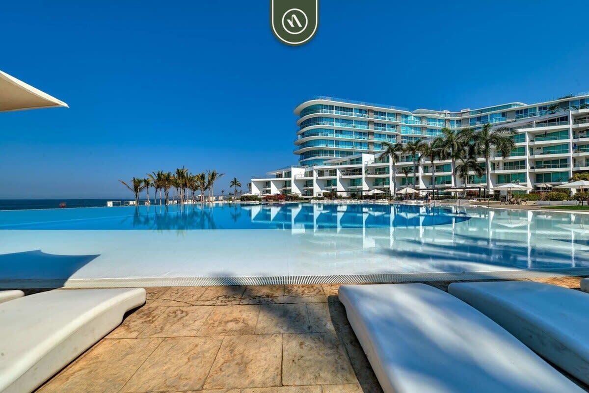A hotel with a large pool, palm trees, and a clear blue sky.