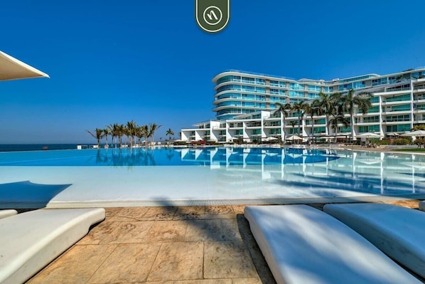 A hotel with a large pool, palm trees, and a clear blue sky.