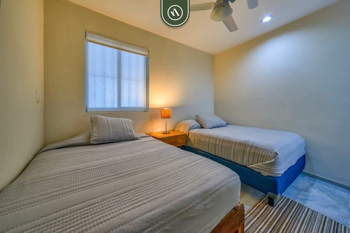 A bedroom with two beds, a window, a nightstand, a lamp, and a ceiling fan.