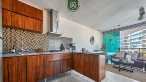 A modern kitchen with wooden cabinets, a tiled backsplash, and a view of a balcony with a pool. - 2BR With Private Balcony - Oceanfront Building (Nuevo Nayarit)
