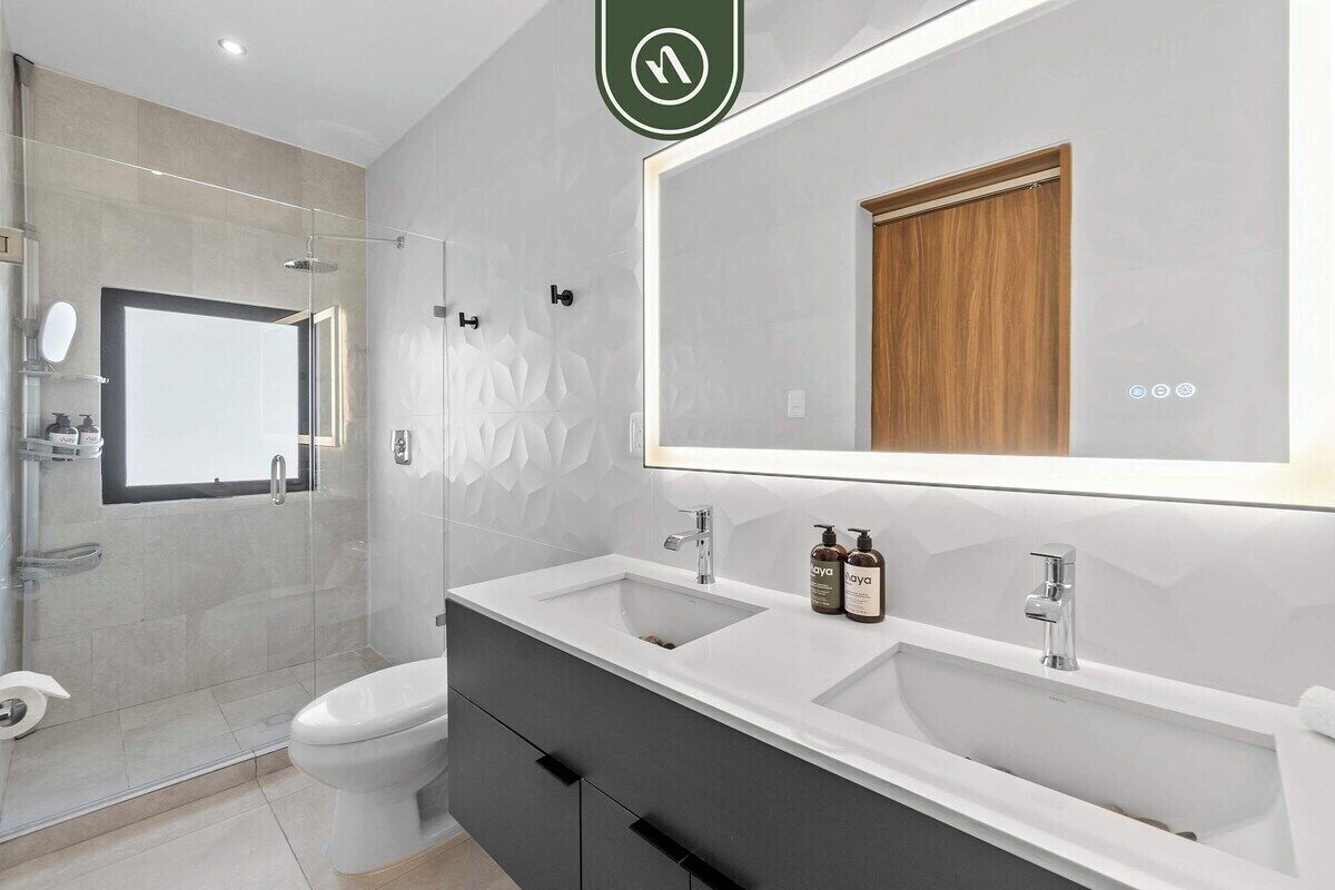 A modern bathroom with a glass shower enclosure, a toilet, a double sink vanity, and a large mirror.