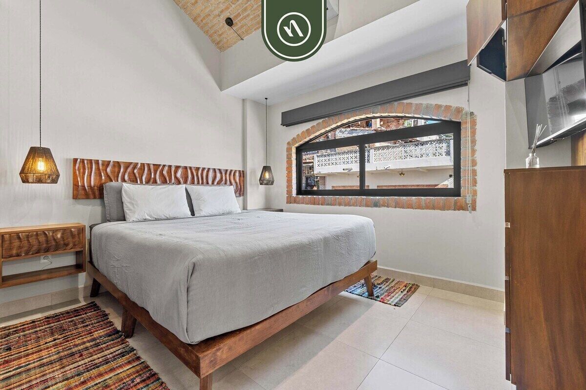 A bedroom with a bed, bedside tables, a window with a view, and a hanging light fixture.