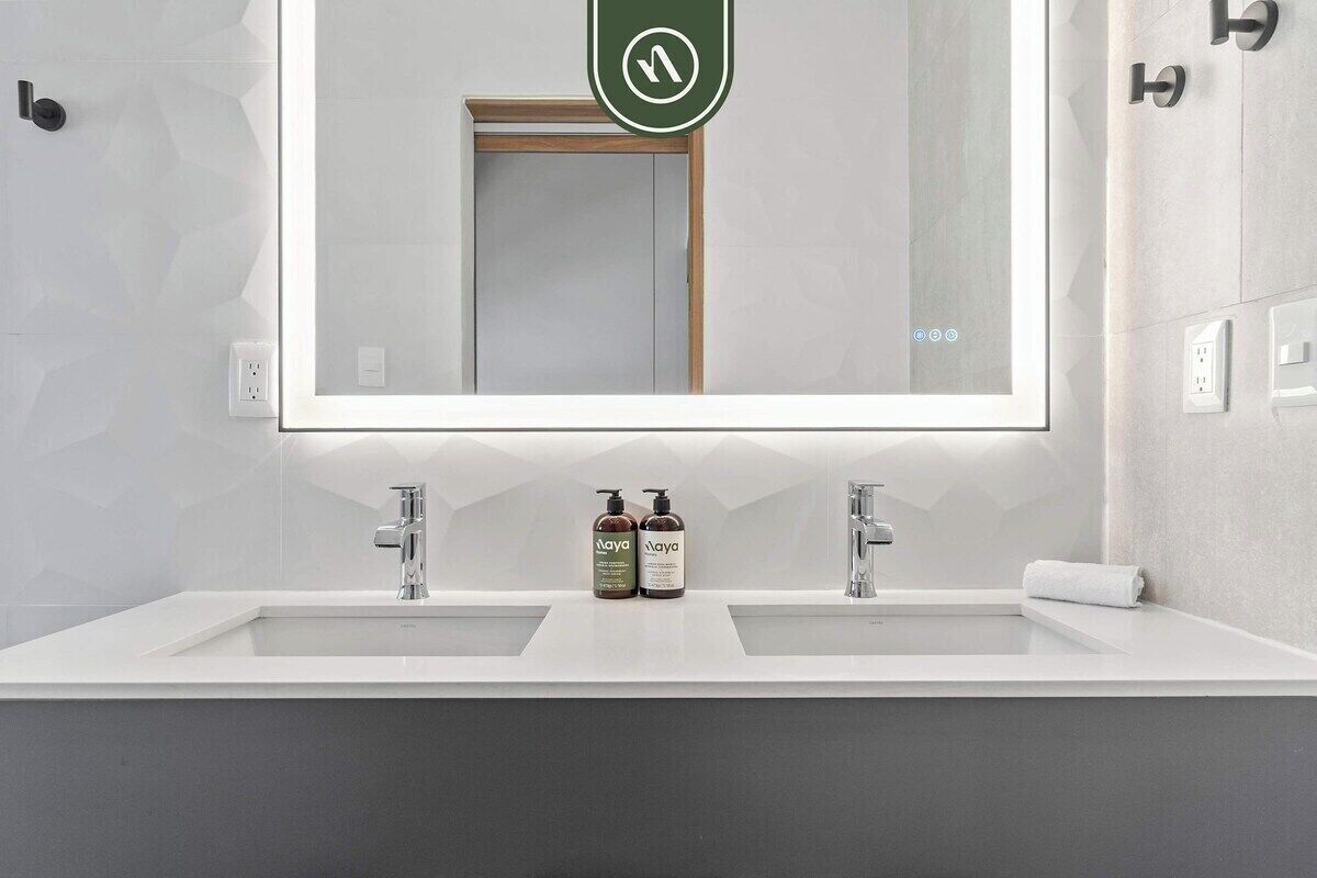 Une salle de bain moderne avec un grand miroir, deux lavabos et un porte-serviettes.
