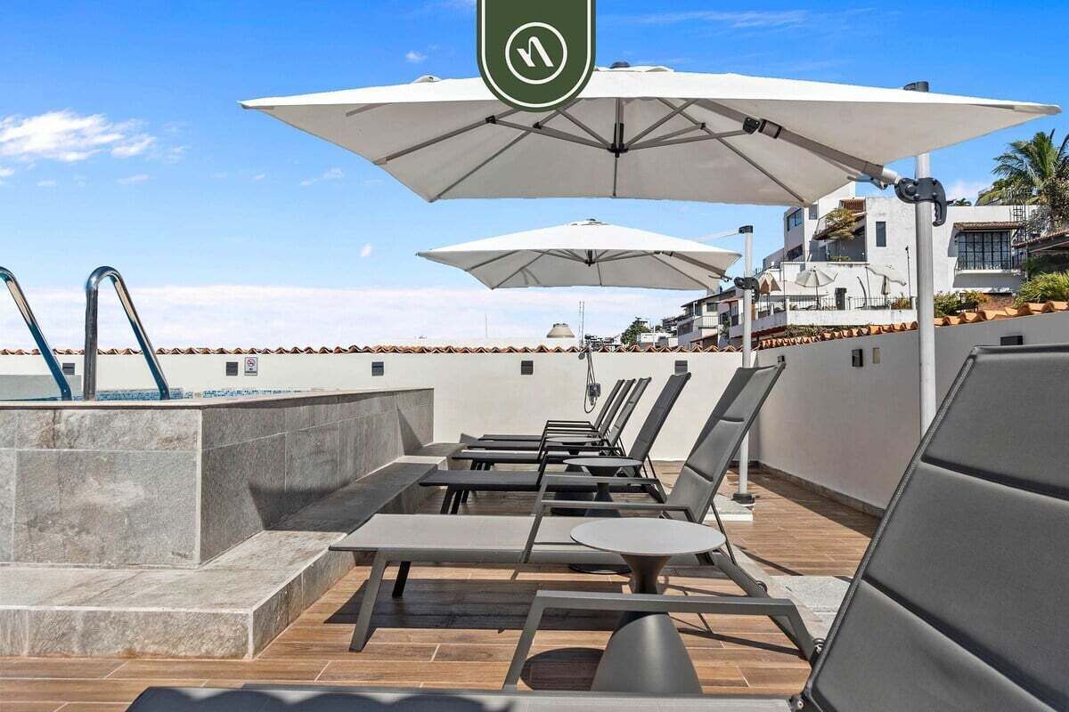 A rooftop pool area with lounge chairs, umbrellas, and a water fountain.