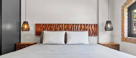 A modern hotel room with a large bed, wooden headboard, two bedside tables, and hanging lamps.