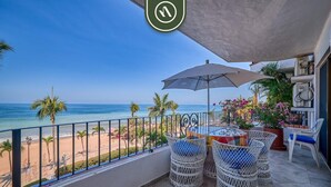 A balcony with a view of the beach, wicker furniture, and a table with a table umbrella.