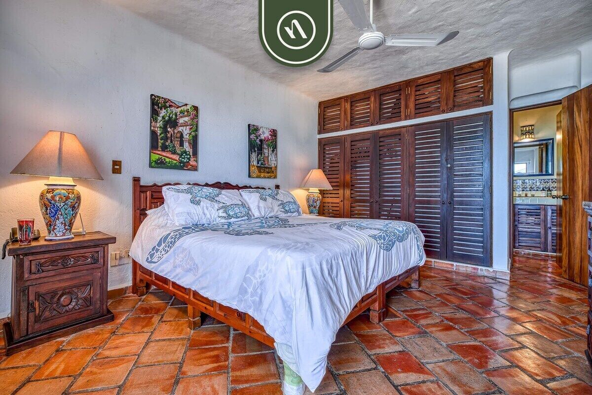 Un dormitorio con cama, contraventanas de madera, ventilador de techo y suelo de baldosas.