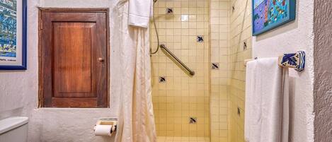 A bathroom with a toilet, a shower with a handrail, a wooden door, and a tiled wall with a painting.