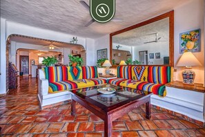 A living room with a colorful sofa, a glass coffee table, and a large mirror.