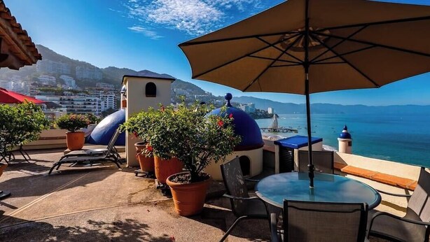 Un patio al aire libre con una mesa, sillas, plantas en macetas y vista al mar.