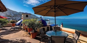 An outdoor patio with a table and chairs, potted plants, and a view of the sea.