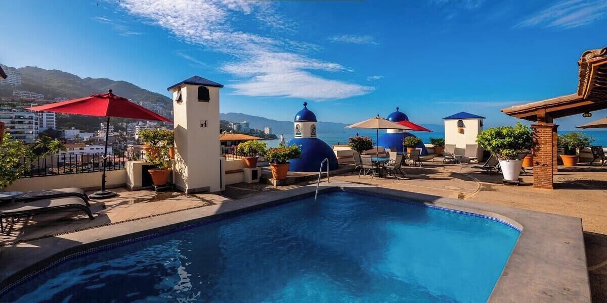 A rooftop pool area with lounge chairs, umbrellas, and potted plants.