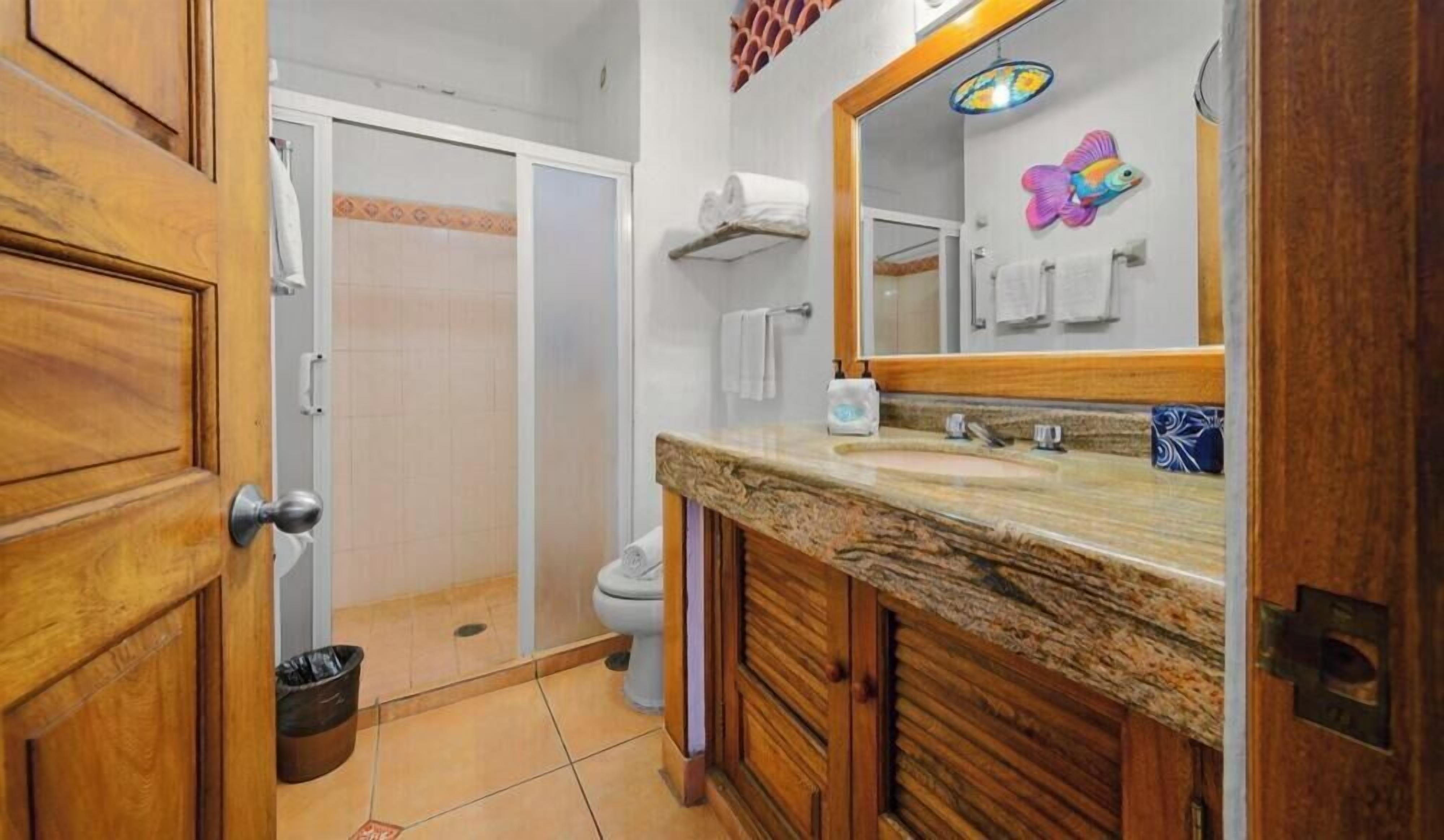 Un baño con tocador de madera, espejo, ducha e inodoro.