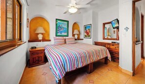 A bedroom with a bed, two bedside tables, a ceiling fan, and framed artwork on the walls.