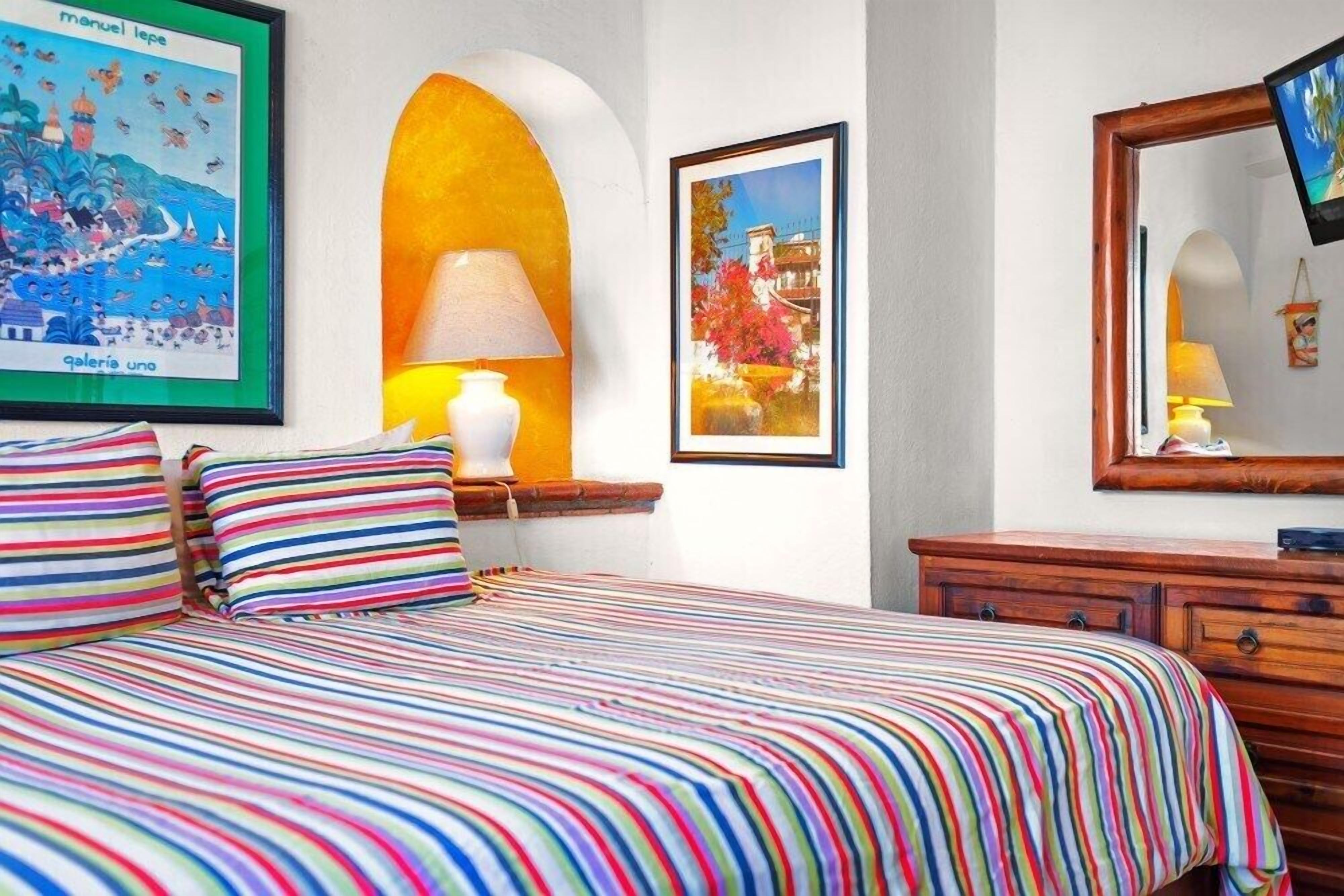 Una habitación de hotel con una cama, una lámpara, un cuadro enmarco y un aparador de madera.