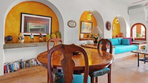 Un comedor con una mesa y sillas de madera, un sofá y un televisor mostrando el letrero de un restaurante de mariscos.