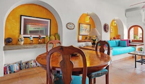 A dining area with a wooden table and chairs, a sofa, and a TV displaying a seafood restaurant sign.
