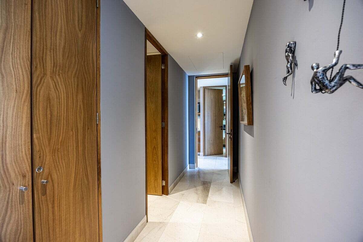 A hallway with wooden doors, a tiled floor, and a wall with two abstract sculptures.