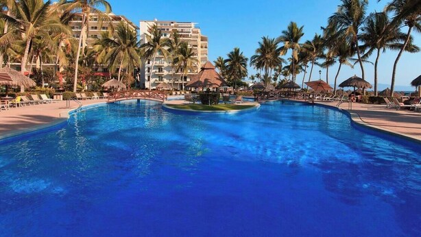 Ein großer Swimmingpool mit Palmen und Liegestühlen, umgeben von einem Hotelgebäude.