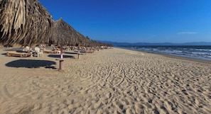A beach with thatched umbrellas and lounge chairs. - Mexican Styled 2 BR Condo - Beachfront - Pool (Nuevo Nayarit)