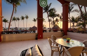 A covered outdoor seating area with a view of palm trees and a beach. - Mexican Styled 2 BR Condo - Beachfront - Pool (Nuevo Nayarit)