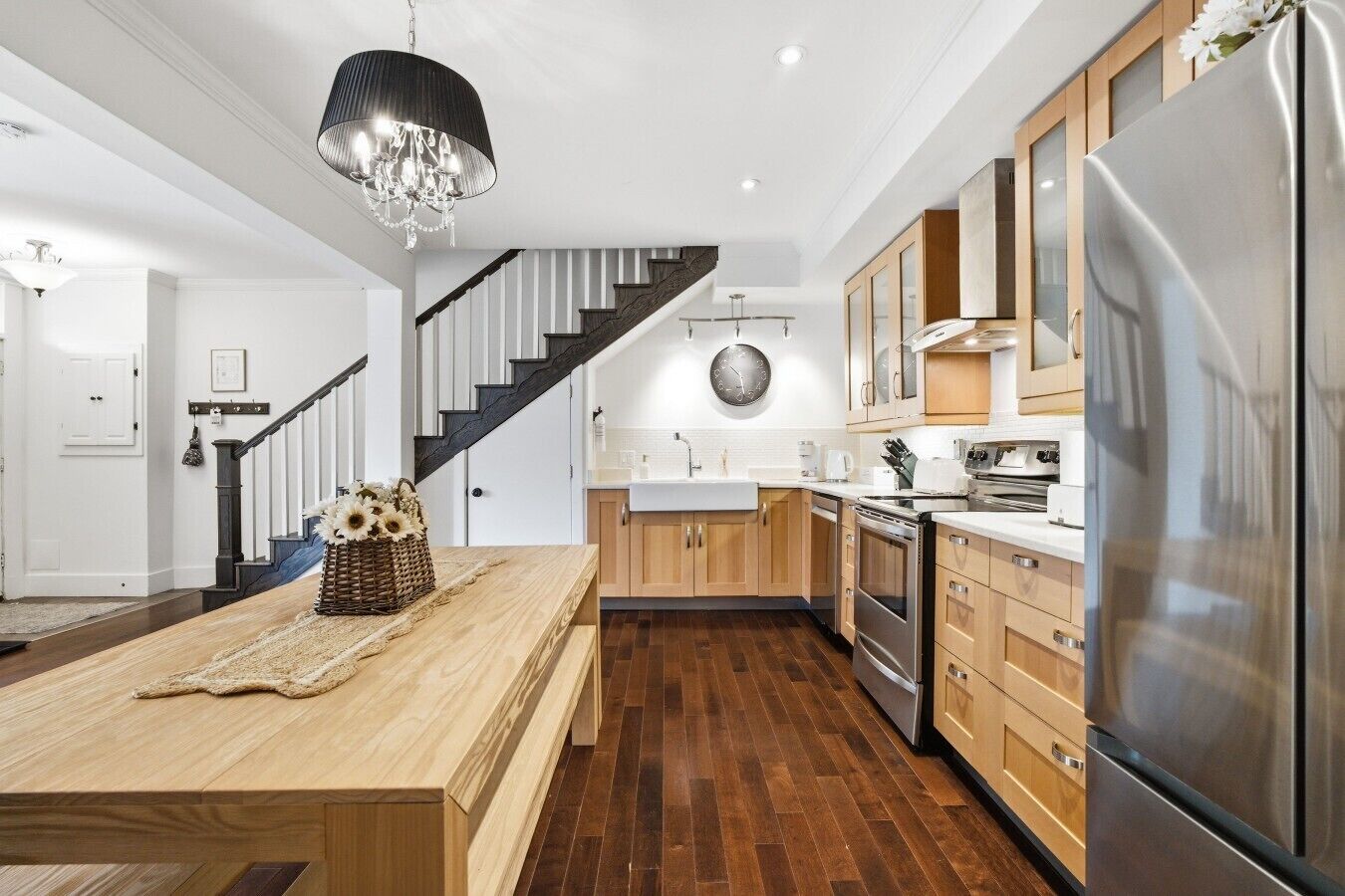 A modern kitchen with a central island, stainless steel appliances, and a wooden staircase.