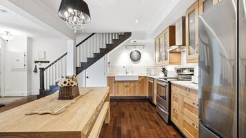 A modern kitchen with a central island, stainless steel appliances, and a wooden staircase.