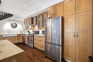 A modern kitchen with wooden cabinets, stainless steel appliances, and a wooden floor. - Spacious Townhouse | 3 BR, Steps to Water St. (St. John`s)