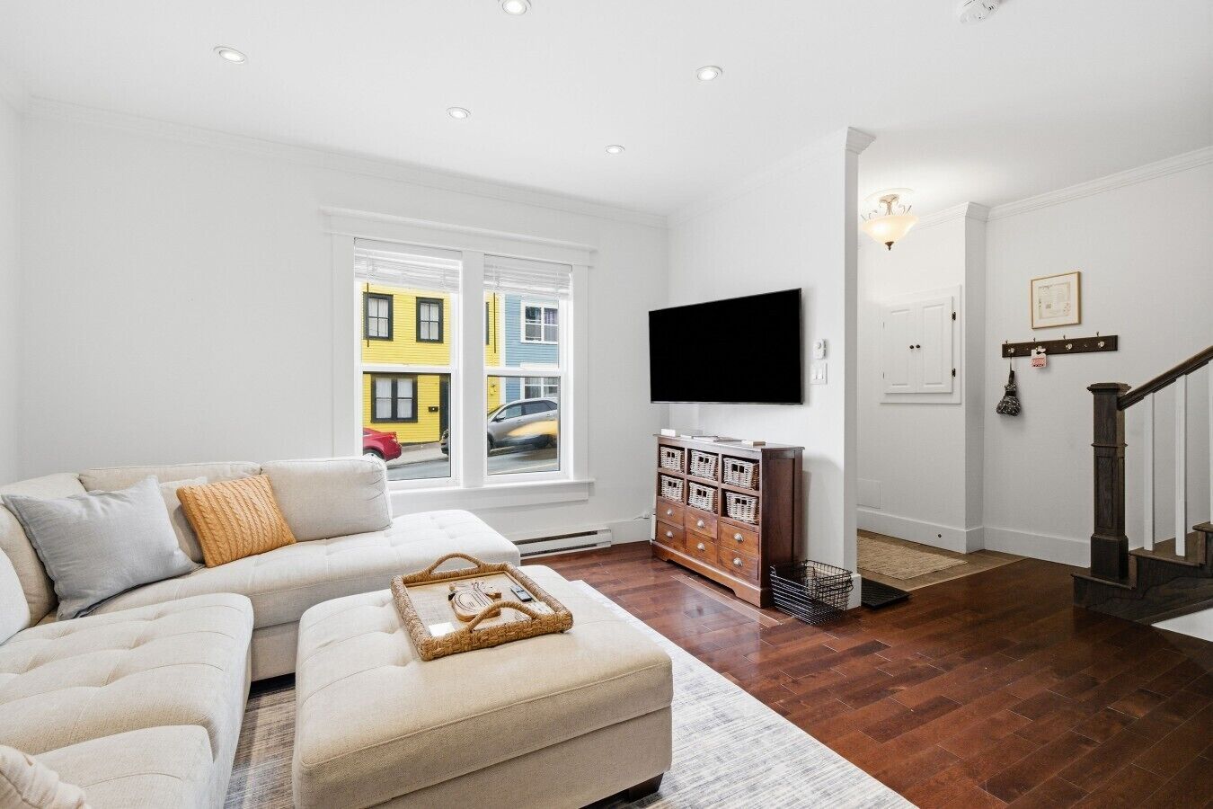 A living room with a sofa, ottoman, and a TV on the wall.