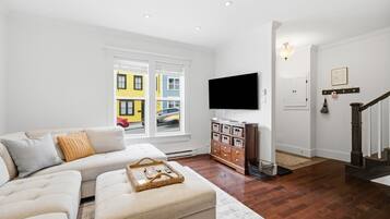 A living room with a sofa, ottoman, and a TV on the wall.