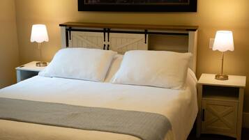 A neatly made bed with two pillows, a bedside table with a lamp, and a nightstand with a lamp.