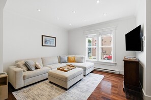 A modern living room with a sofa, ottoman, and a flat-screen TV. - Spacious Townhouse | 3 BR, Steps to Water St. (St. John`s)