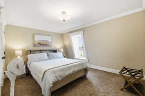 A bedroom with a bed, bedside lamps, a ceiling fan, a window with a view, and a wooden chair. - Spacious Townhouse | 3 BR, Steps to Water St. (St. John`s)