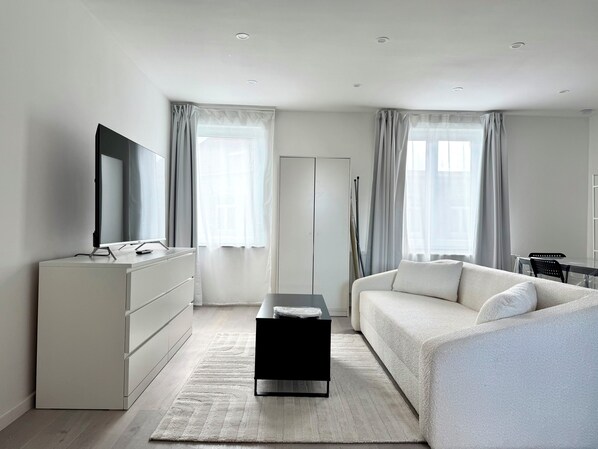A modern bedroom with a bed, a desk, a dresser, and a TV.
