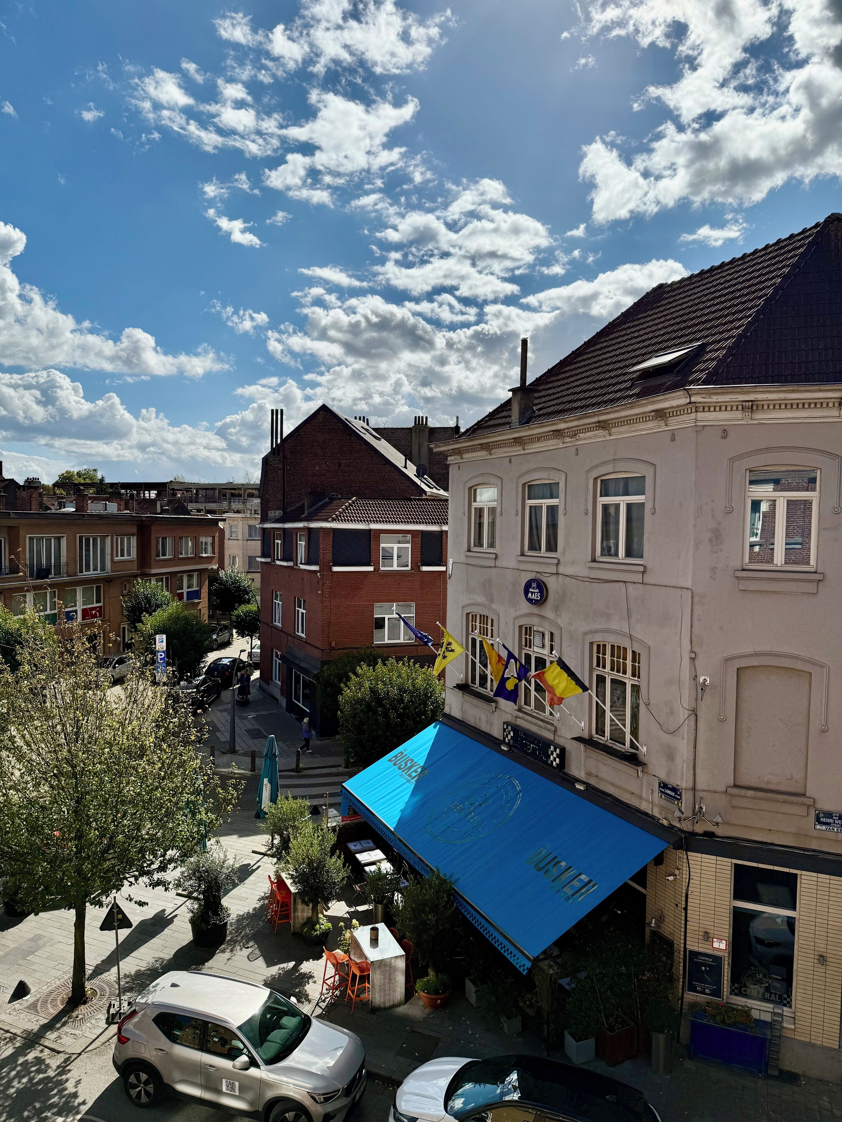 Straatbeeld met gebouwen, een blauw luifel en een geparkeerde auto.