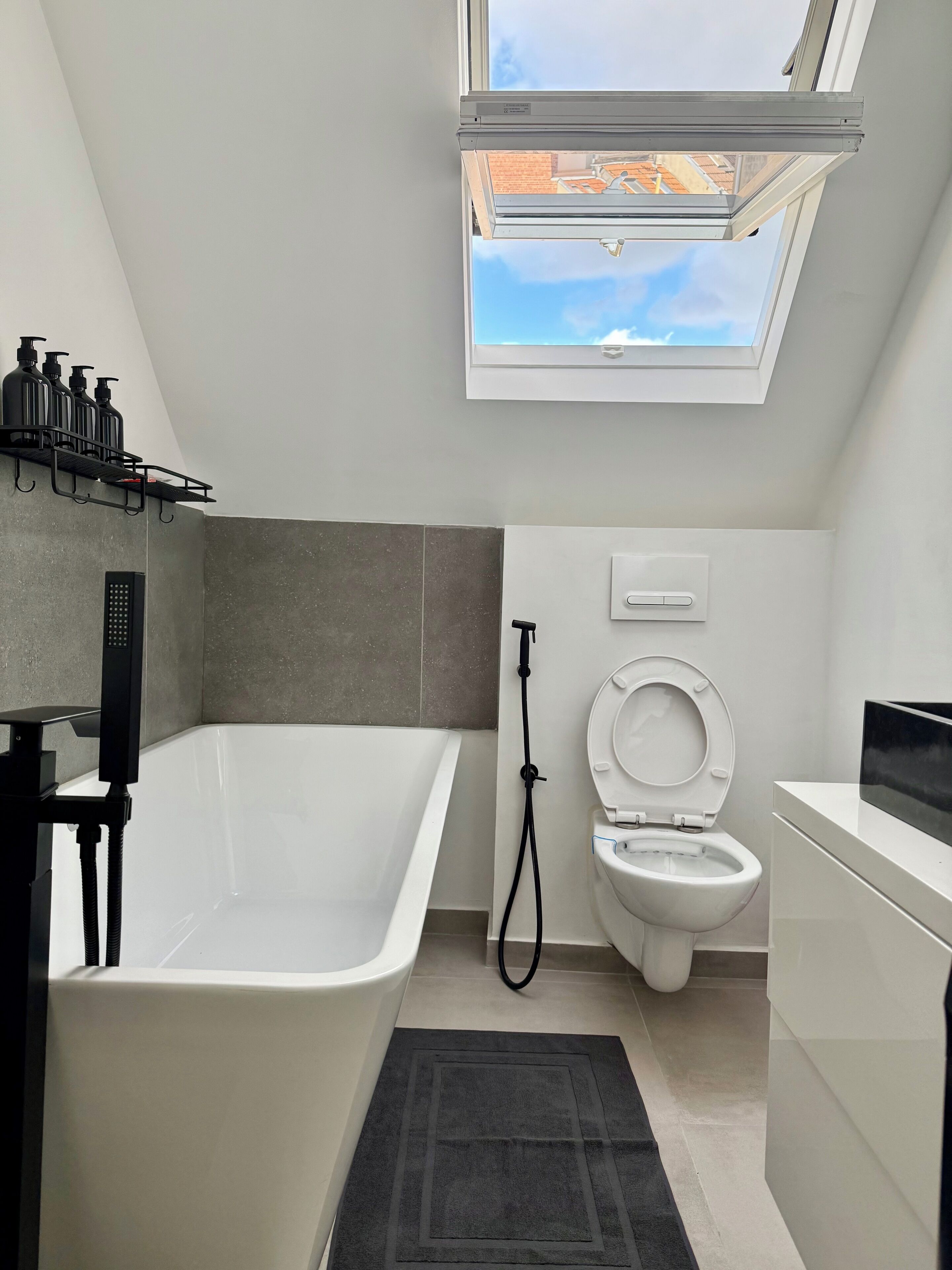 A modern bathroom with a freestanding bathtub, a toilet, and a shower. There is a skylight above the toilet.