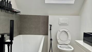 A modern bathroom with a freestanding bathtub, a toilet, and a shower. There is a skylight above the toilet.