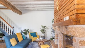 Een woonkamer met een blauwe bank, gele kussens, een houten salontafel en een stenen openhaard.