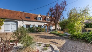 Een huis met een pannendak, een garage en een tuin met diverse planten en een pergola.