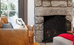 Una sala de estar acogedora con chimenea de piedra, sofá de cuero y vistas al verdor exterior.