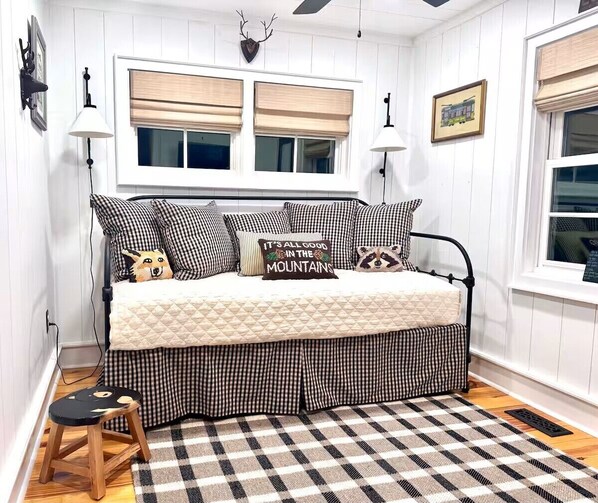 A bed with checkered bedding, a quilted blanket, and decorative pillows, including one with a mountain design.