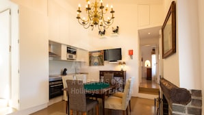A dining area with a table and chairs, a television mounted on the wall, and a chandelier.