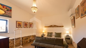 A cozy bedroom with a bed, bedside lamps, a stone wall, and a hanging light fixture.